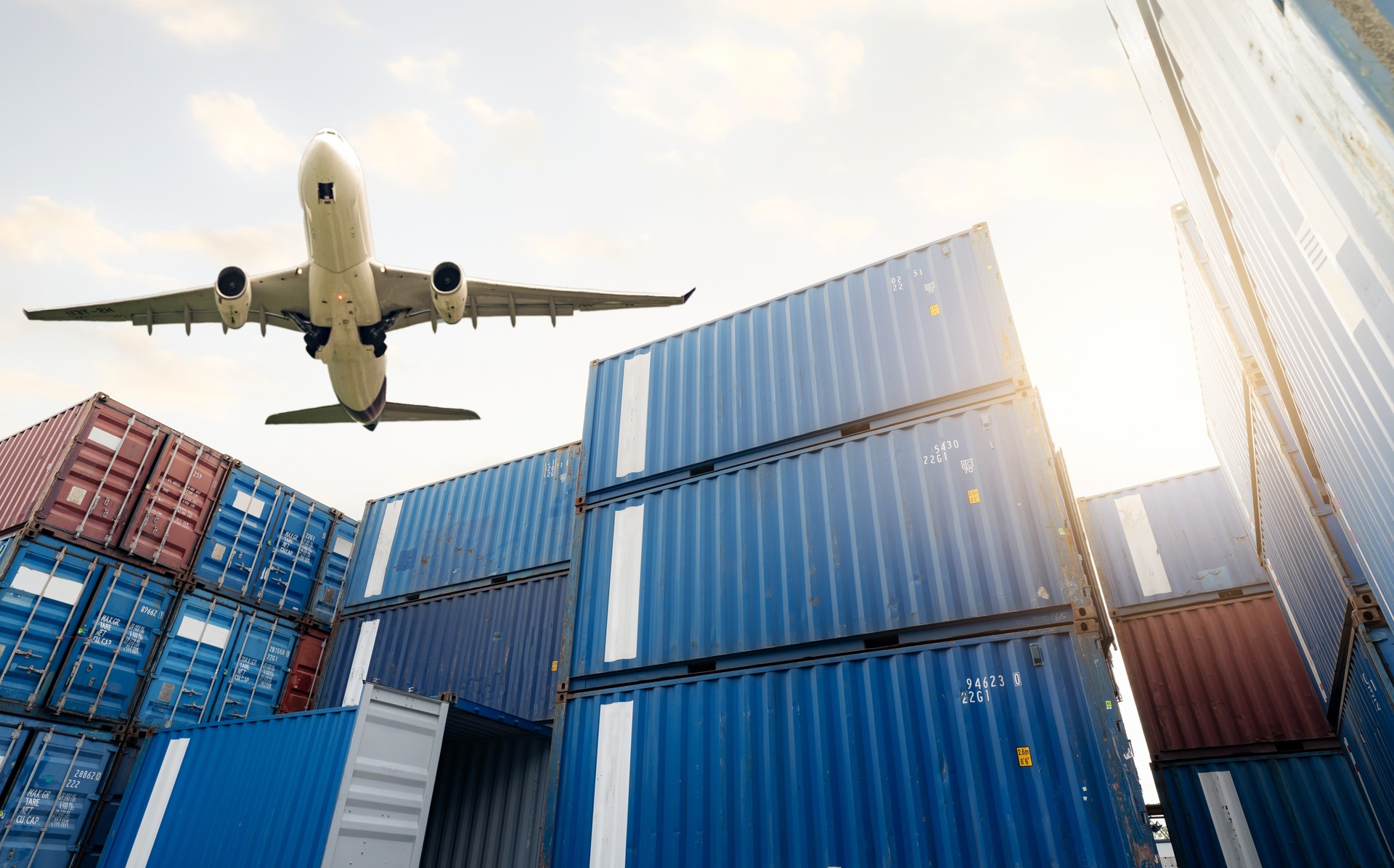 Air logistics. Cargo airplane flying above stack of logistic container. Cargo and shipping business. Container ship for export logistic. Logistic industry from port to port. Freight transportation.